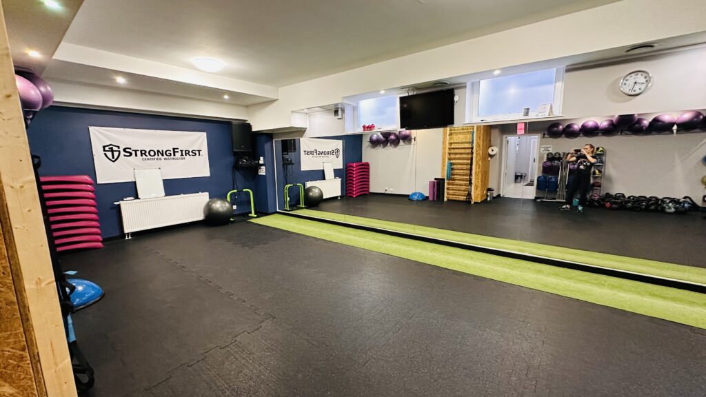 Zdjęcie ukazuje wnętrze sali fitness w siłowni strongbodygym, gdzie widzimy wielkie lustro oraz odbijające się w nim pomoce do ćwiczeń.